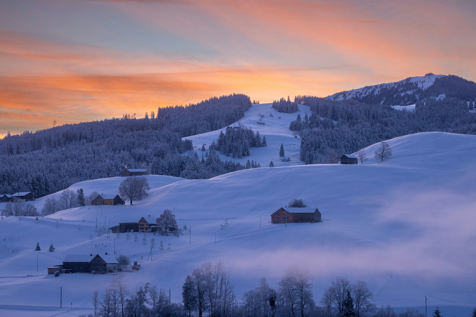 Sunset glowing over a snow-covered alpine village beneath forested peaks