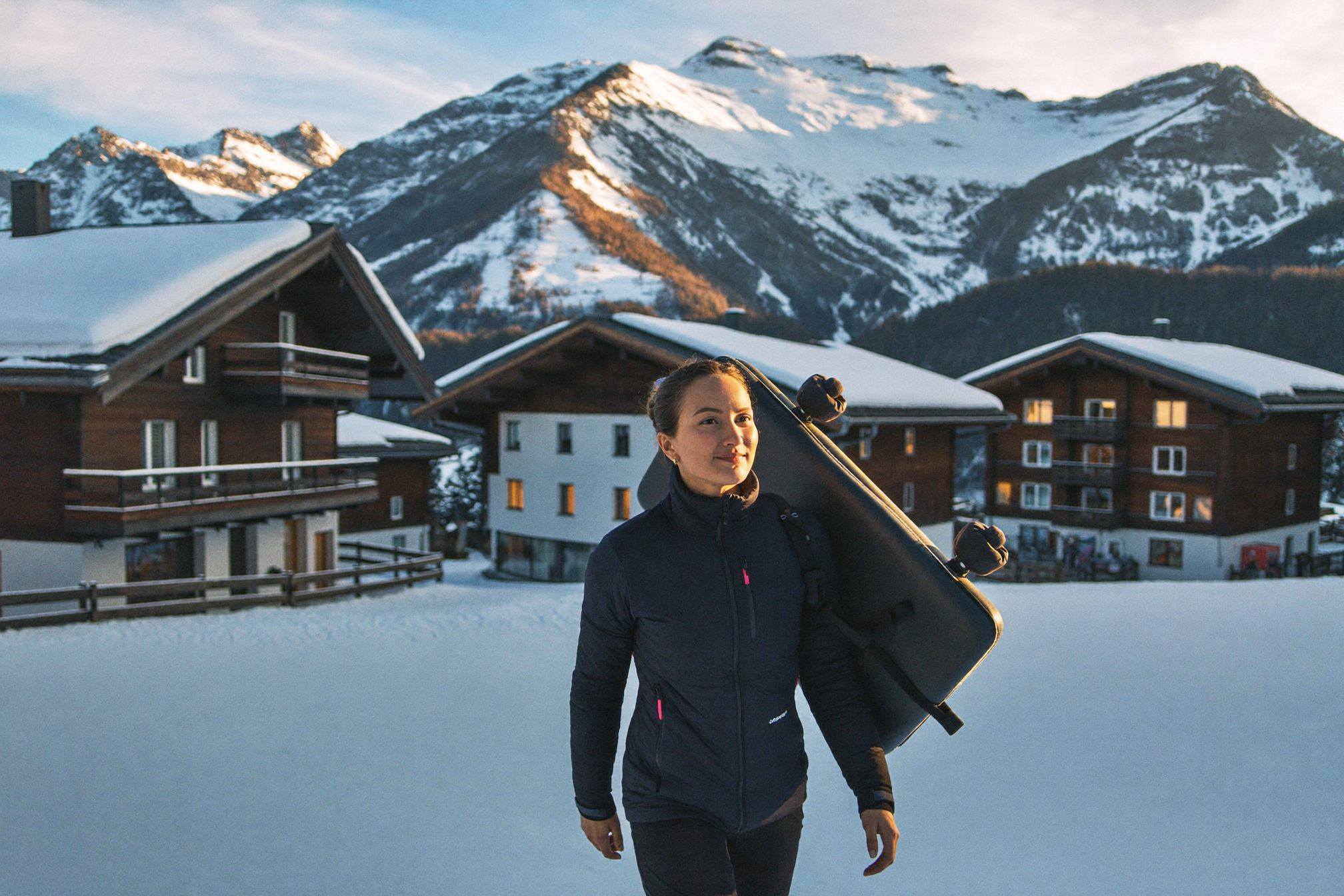 Therapist carrying a mobile treatment table through a snowy Les Arcs village at sunset